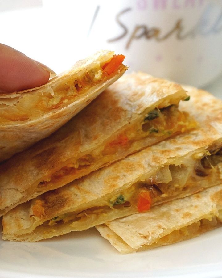 Hand holding Stacked Masala Scrambled Egg Quesadillas on a plate
