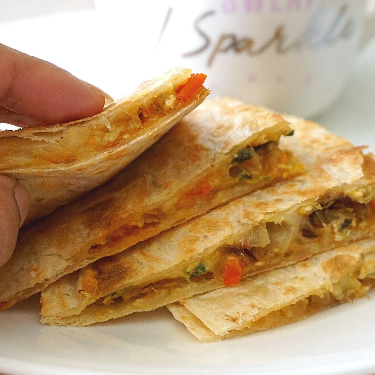 Hand holding Stacked Masala Scrambled Egg Quesadillas on a plate