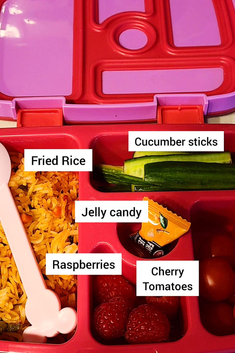 Lunchbox with fried rice, cucumber, tomatoes, raspberries and candy.