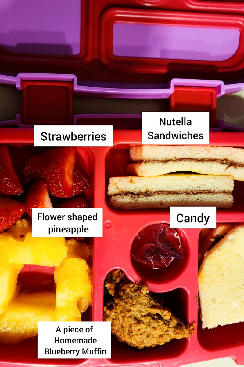 Lunchbox with nutella sandwich, strawberries, candy, muffin and pineapple.