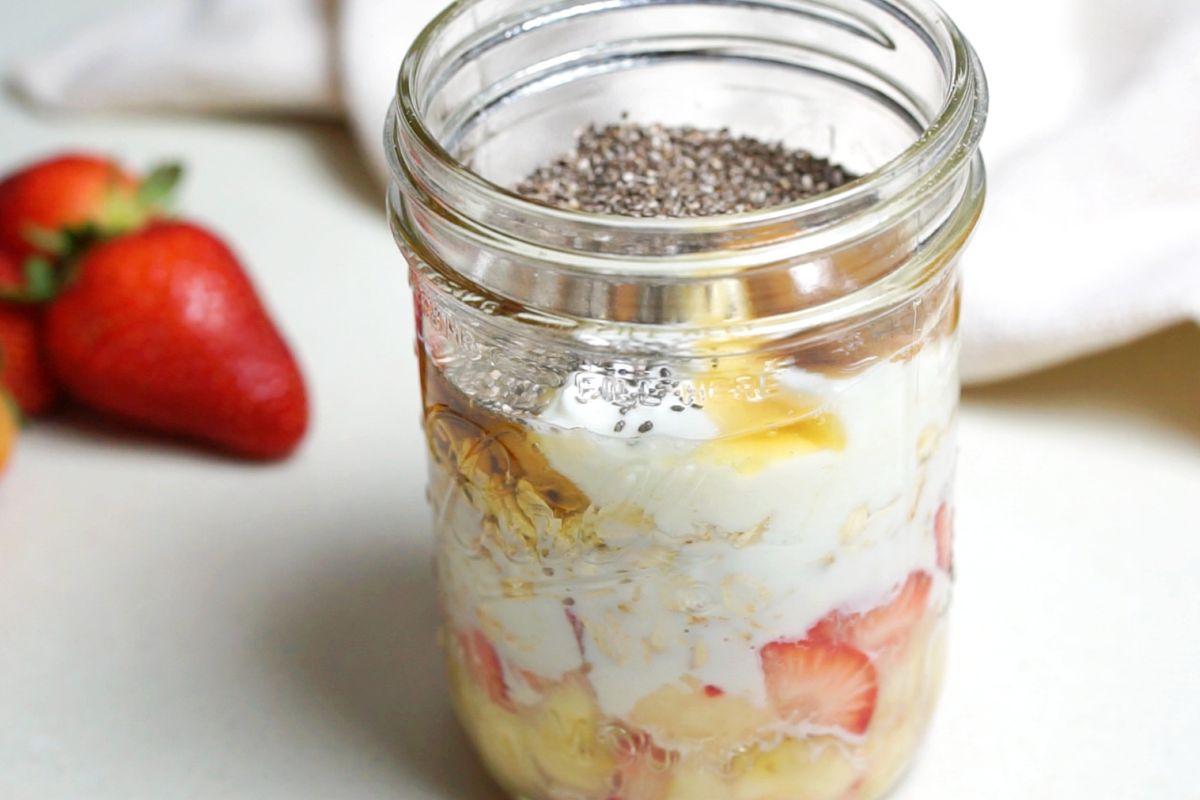 Overnight oats jar with chopped fruits, milk, yogurt, chia seeds and other ingredients.